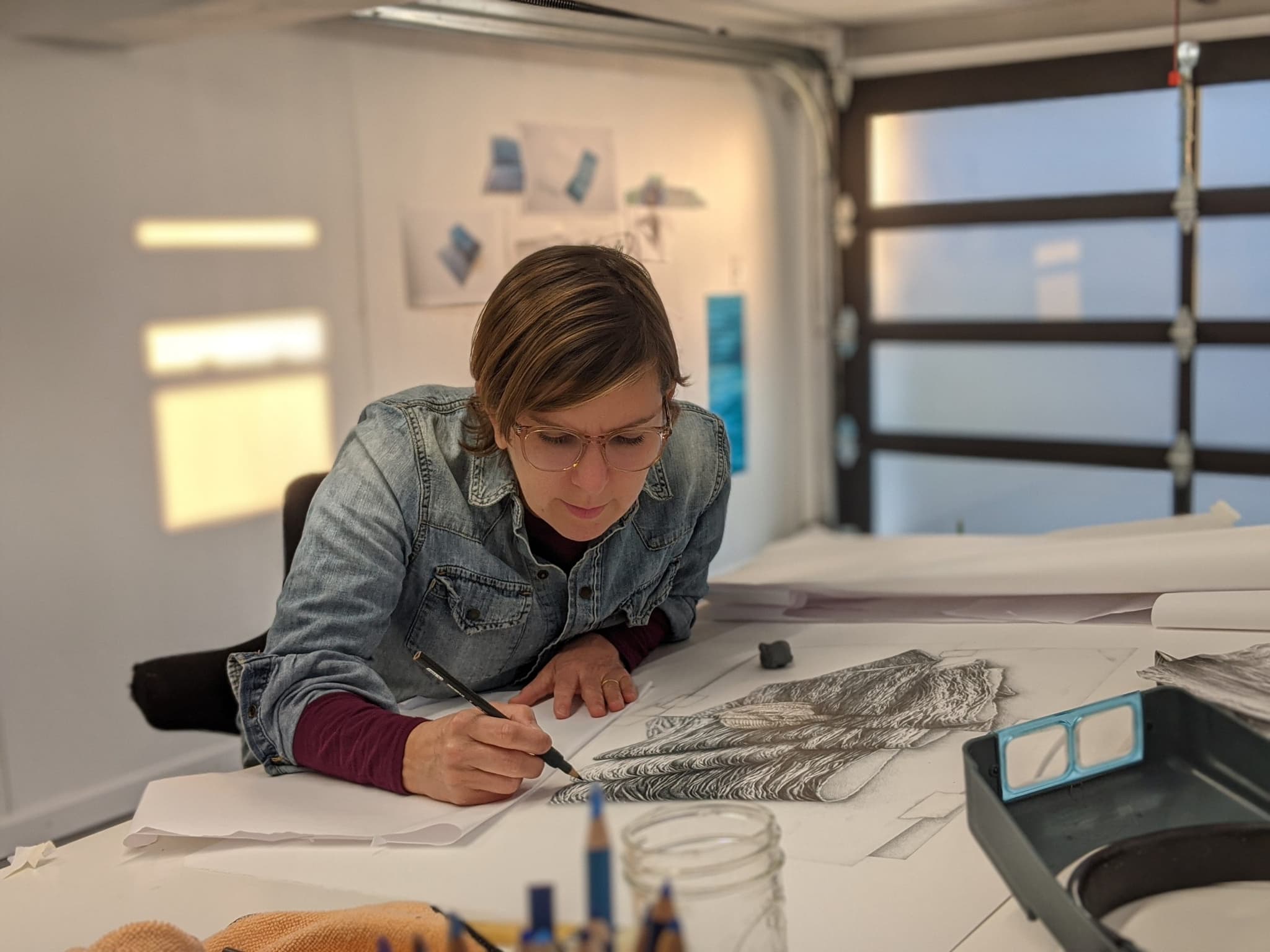 Evelyn Rydz is wearing a denim jacket, hunched over a work of art she is developing in her studio.
